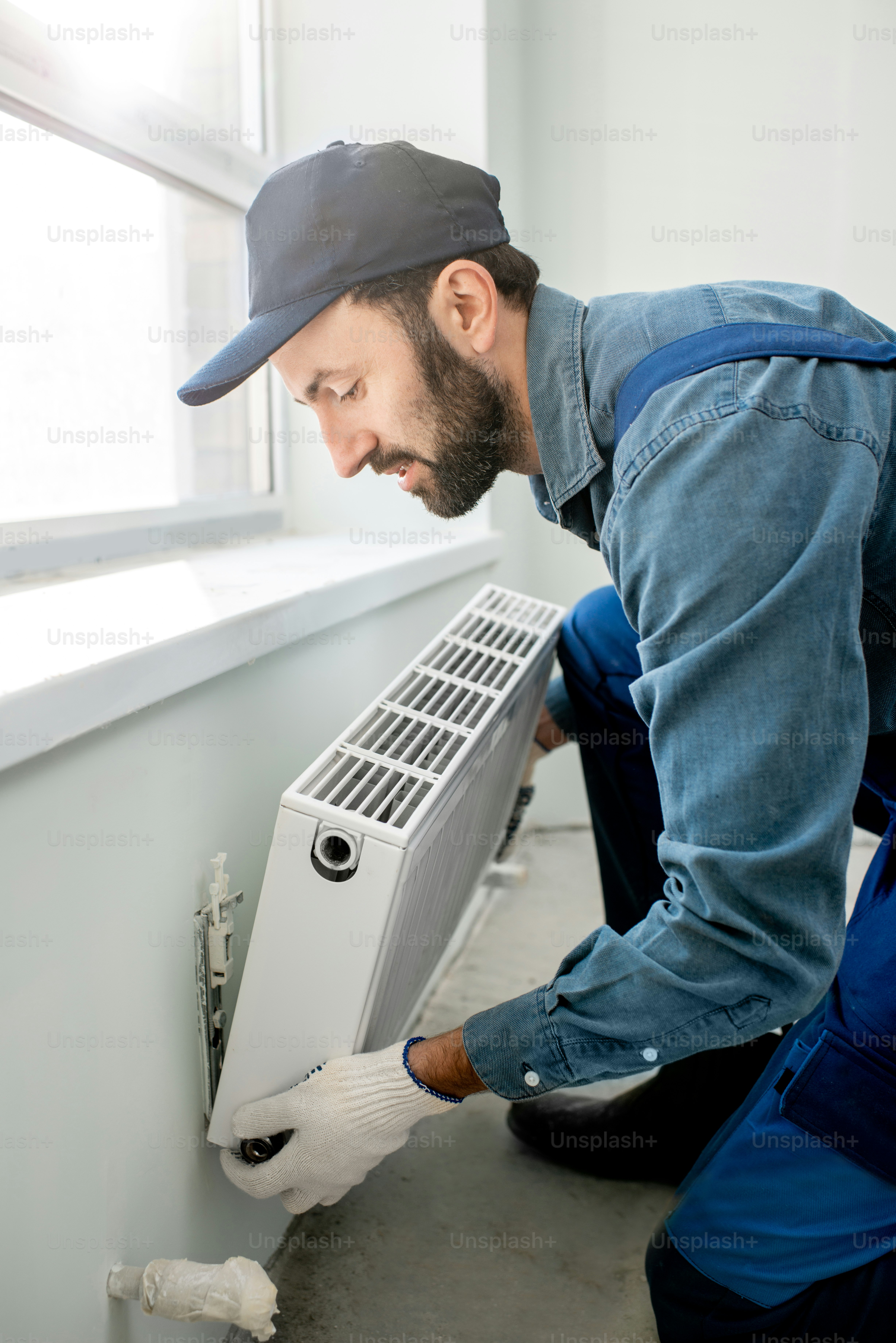 Workman mounting water heating radiator near the window in the white renovated living room